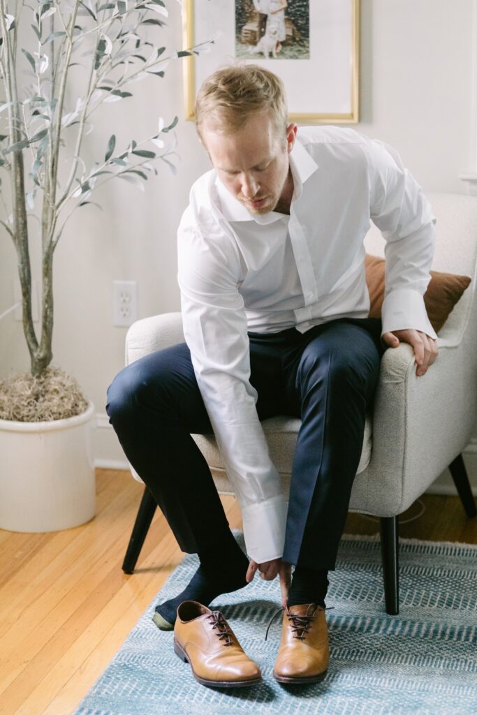 Groom putting on his shoes at his parent's house on the morning of a spring wedding near Philadelphia
