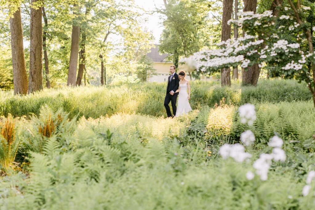 Bride and groom walking through ferns on a verdant spring wedding day near Philadelphia