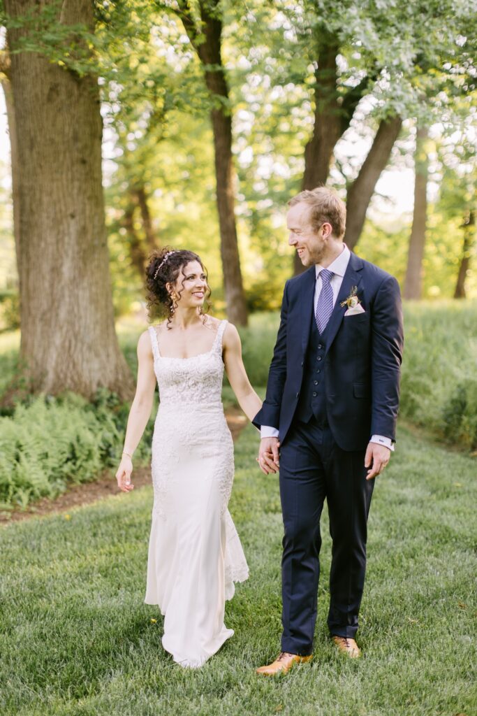Bride and groom holding hands and walking during golden hour portraits on a bright spring wedding day near Philadelphia