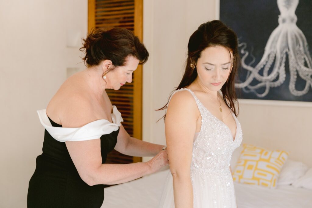 Mother of the bride helping button the wedding gown while getting ready for a modern destination wedding