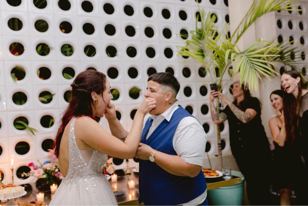 Lesbian couple feeding each other wedding cake at their vibrant tropical destination wedding reception