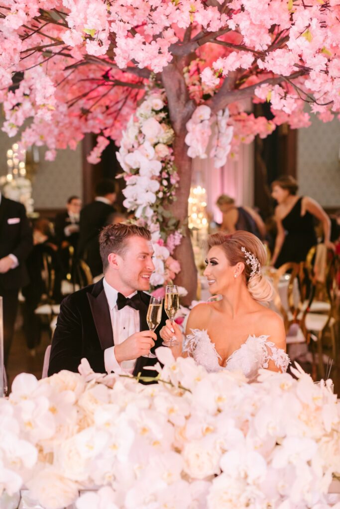 Bride and groom cheers under a cherry blossom inspired floral installation at a wedding reception
