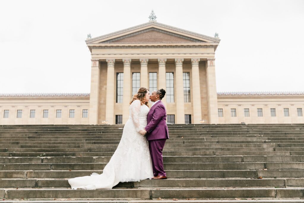 Brides kissing on the steps of the Philadelphia Art Museum by Emily Wren Photography