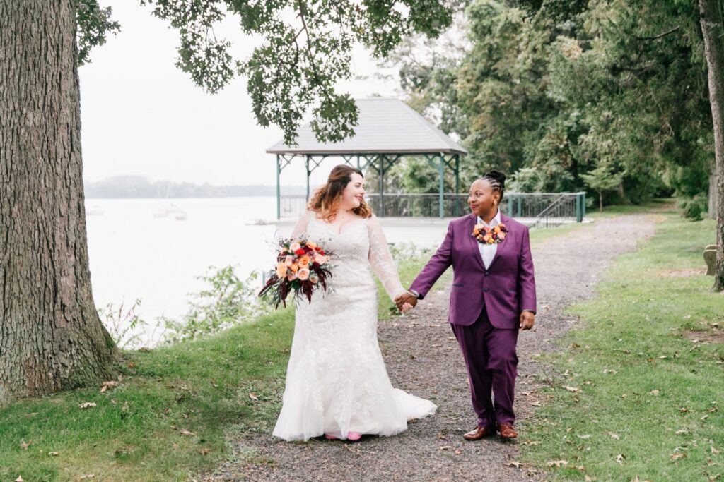 LGBTQ couple holding hands at walking along the Delaware River on their wedding day at Glen Foerd