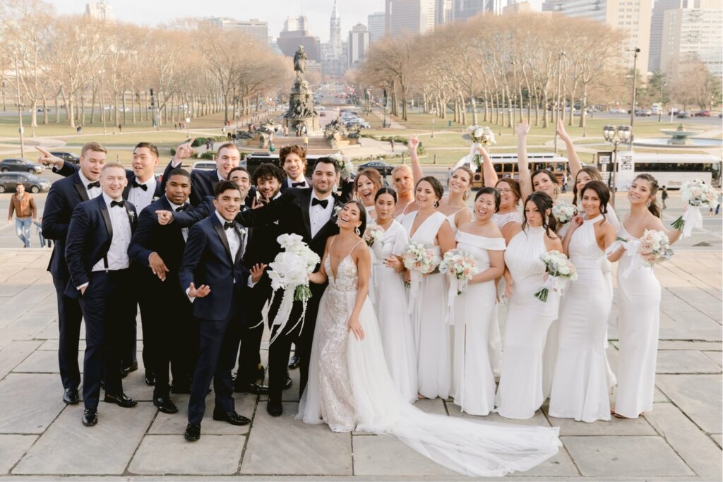 Wedding party cheering on the steps of the Art Museum with the Philadelphia skyline behind them