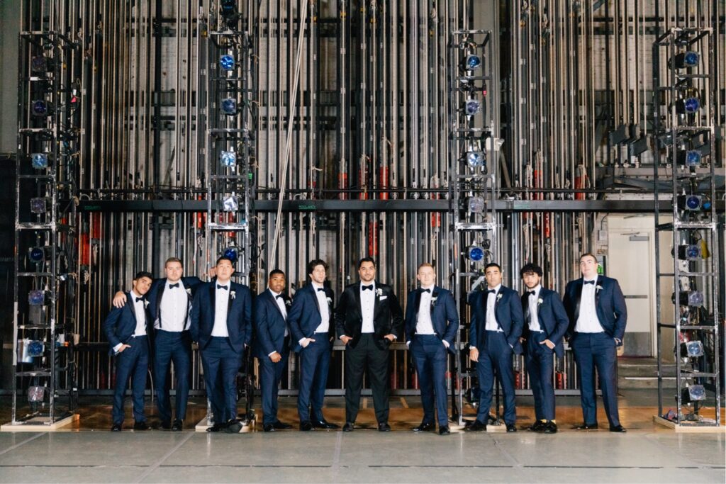 Groom and groomsmen with stage rigging behind them at the Academy of Music