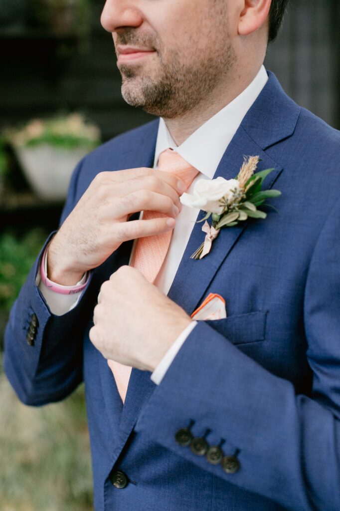 Groom adjusting his peach tie while getting ready for a intimate wedding ceremony