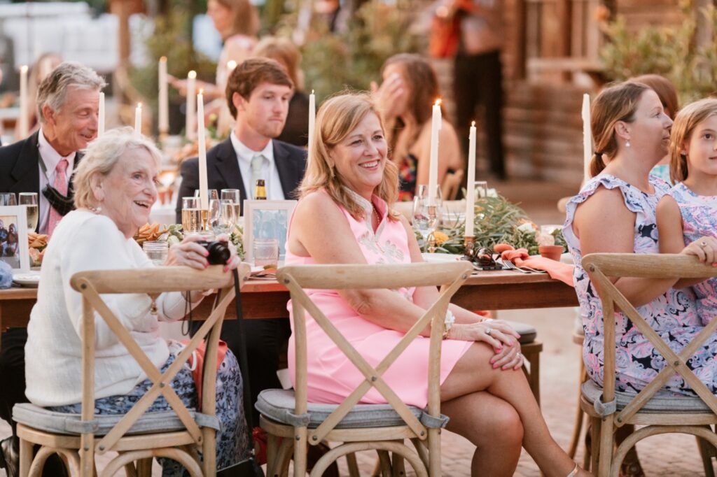 Wedding guests laugh as they listen to speeches during an intimate garden wedding reception
