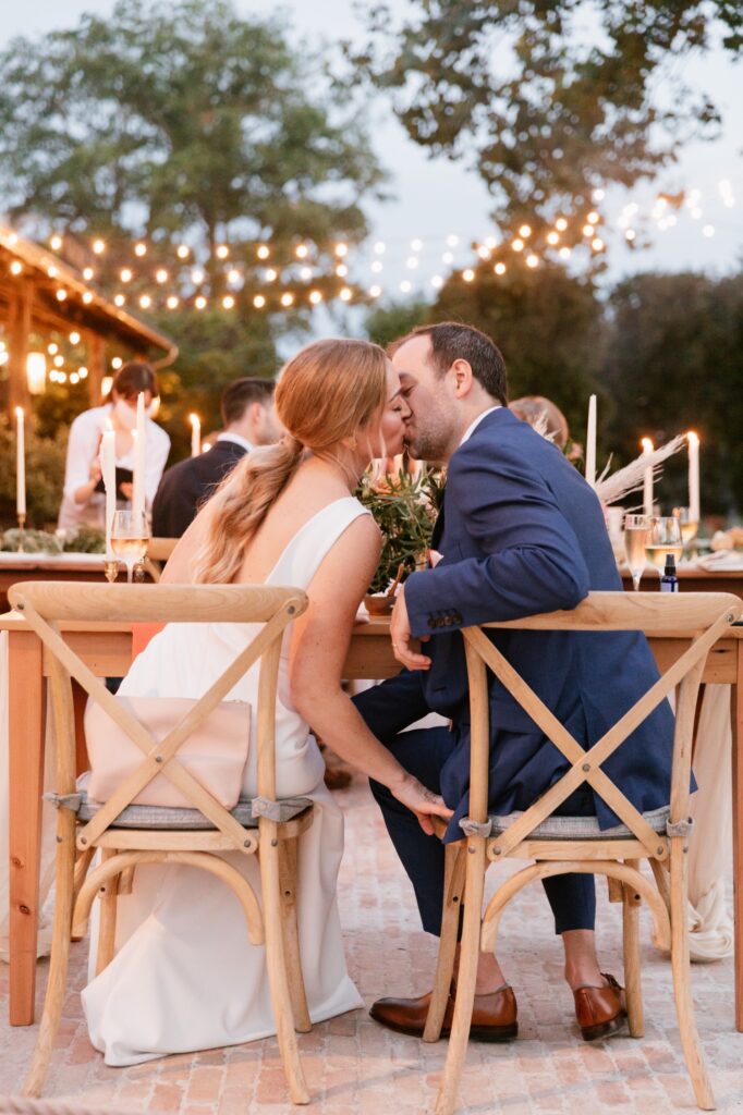 Bride and groom kiss under twinkle lights at an outdoor garden wedding reception on a summer day near Philadelphia