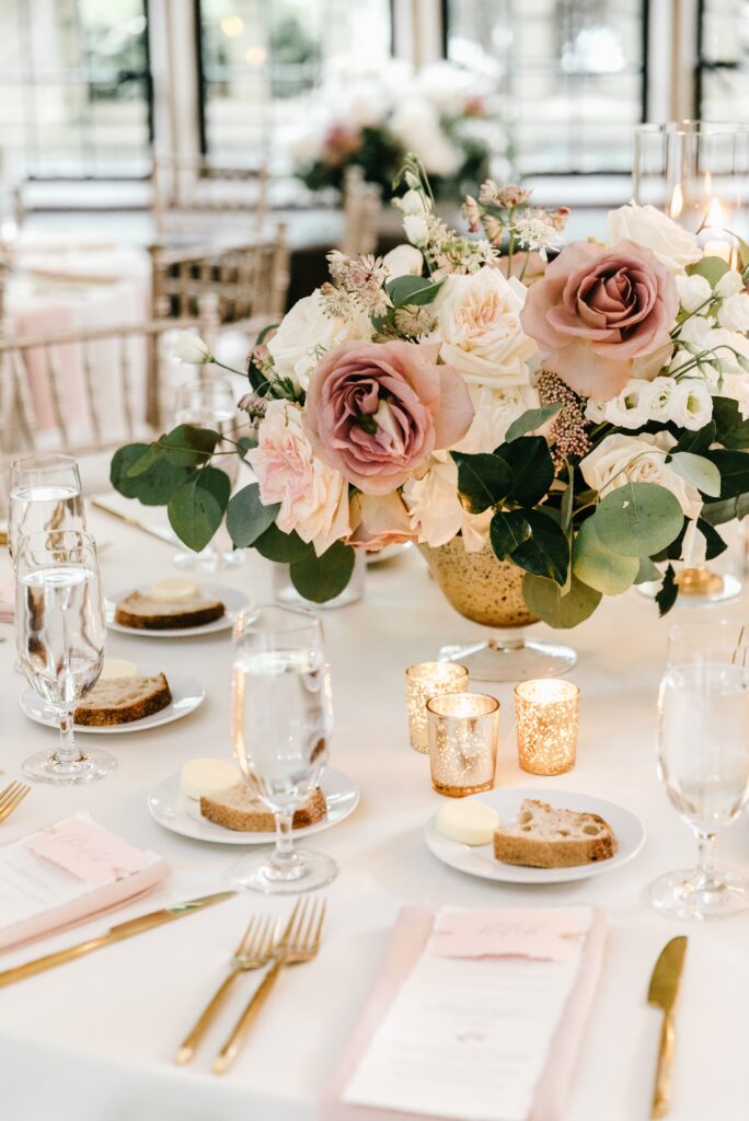 Low floral centerpiece with gold votive candles at a romantic wedding reception