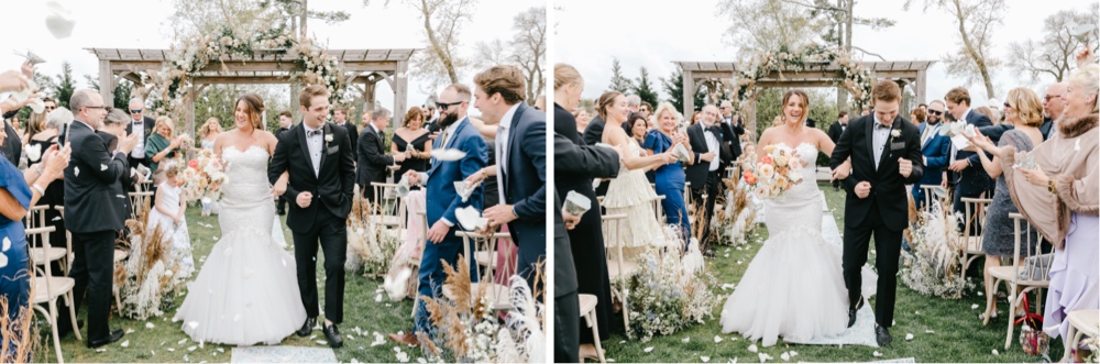 Wedding guests throw flower petals as the newlyweds walk down the aisle after an outdoor wedding ceremony