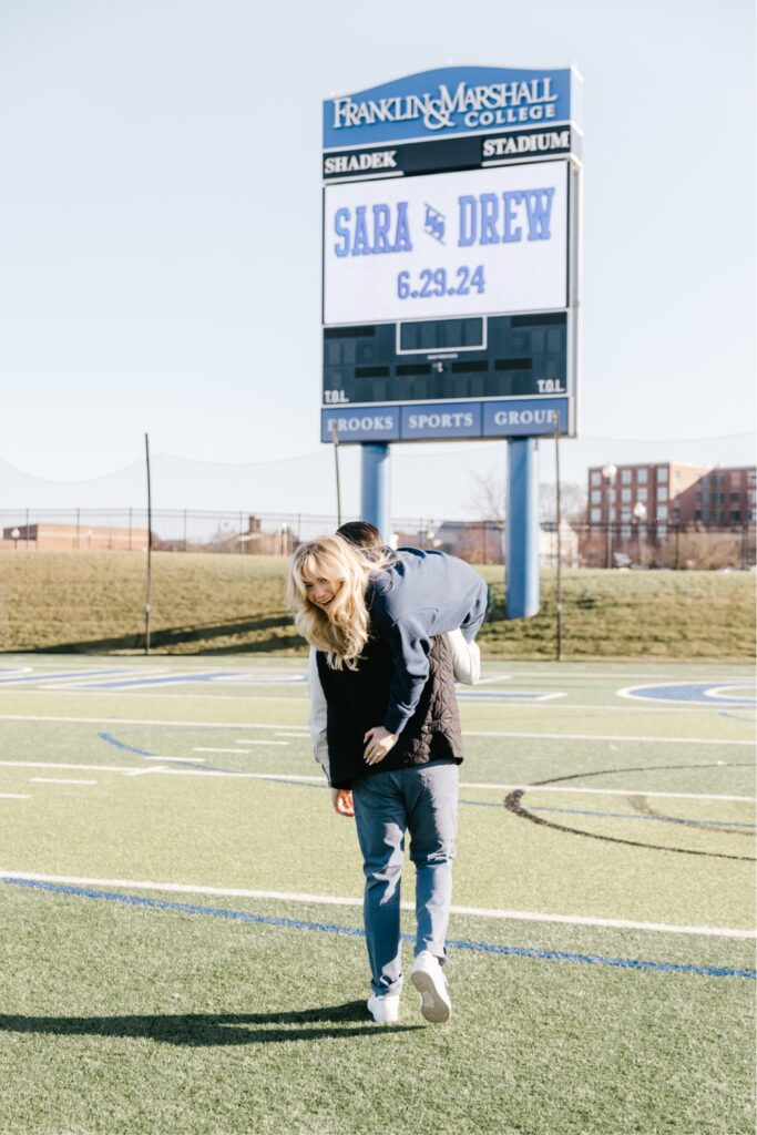 Man carrying his fiancee across the football field at Franklin & Marshall college during and engagement session