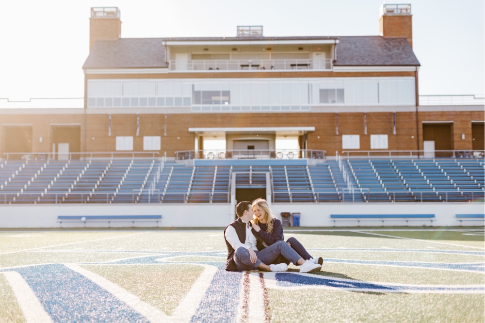 Engaged couple sitting and laughing on a football field during a portrait session near Philadelphia