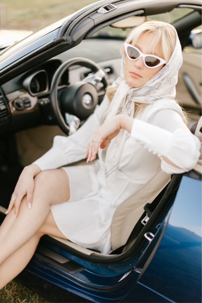 Bride sitting in a timeless convertible car with vintage sunglasses during a sunset engagement portrait session