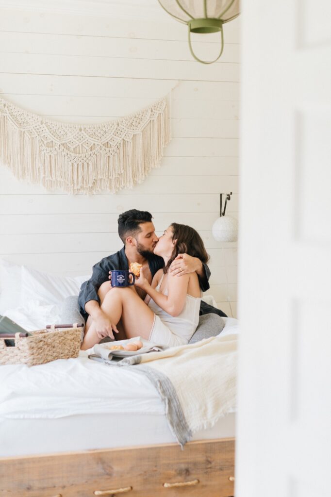 Couple kissing while eating breakfast in bed at Foxfire Mountain House's suite in New York