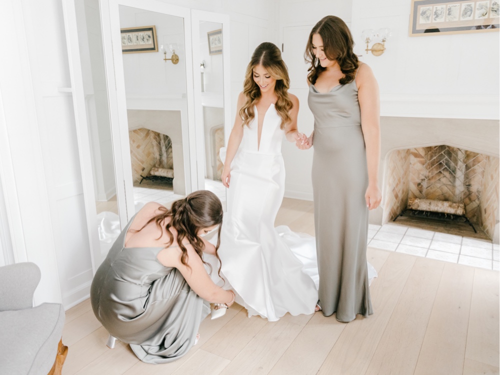 Bridesmaids helping the bride put on her wedding shoes while getting ready for a spring wedding day