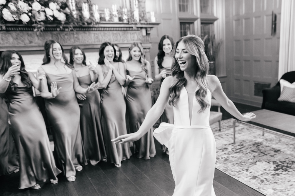Bride and bridesmaids laugh with joy after the bride reveals her wedding dress