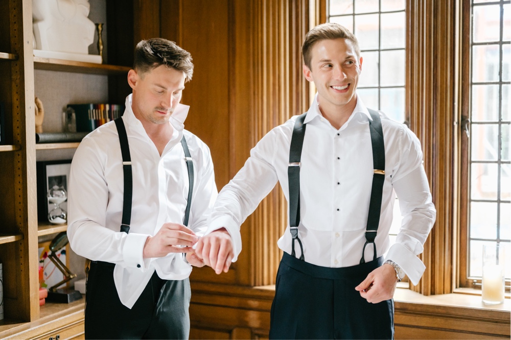 Groomsmen helps the groom with his cufflinks while getting ready for a spring wedding celebration