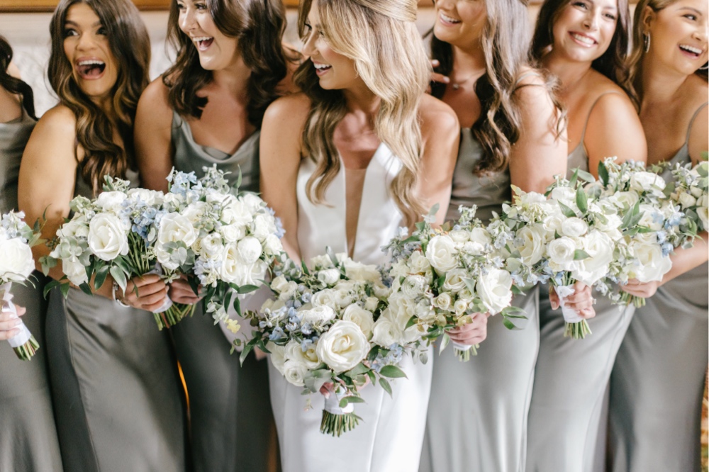 Bride and bridesmaids laughing with spring bouquets on a rainy wedding day in New Jersey