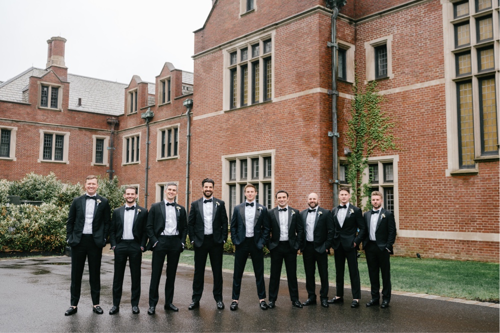 Groom and groomsmen in front of a regal brick building on a spring wedding day at Natirar