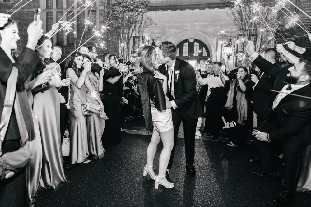 Bride and groom kiss during their sparkler exit as guests cheer by Emily Wren Photography