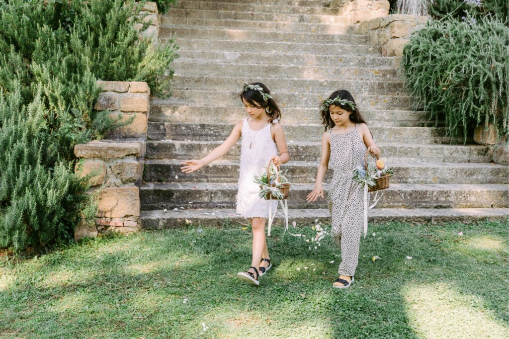 Flower girls in olive branch crowns tossing petals during a summer wedding ceremony in Tuscany