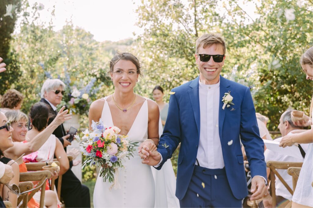 Newlyweds smiling as guests throw flower petals at a destination wedding ceremony in Italy