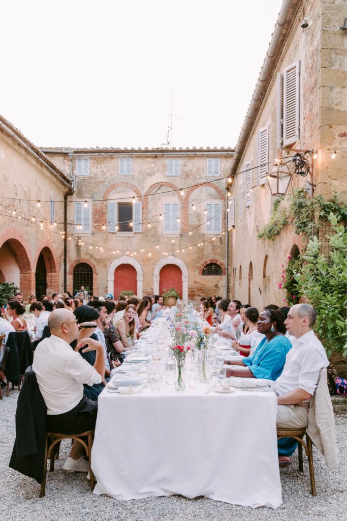Guests seated at long tables under twinkle lights at a destination wedding in Tuscany