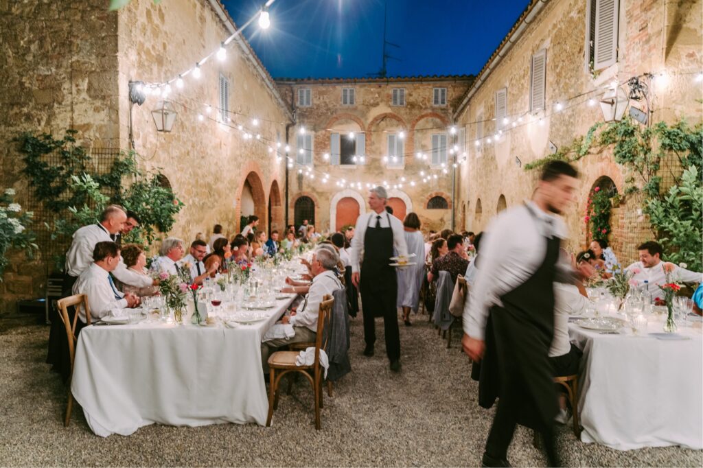 Wedding guests being served dinner al fresco under twinkle light at the Borgo Estate