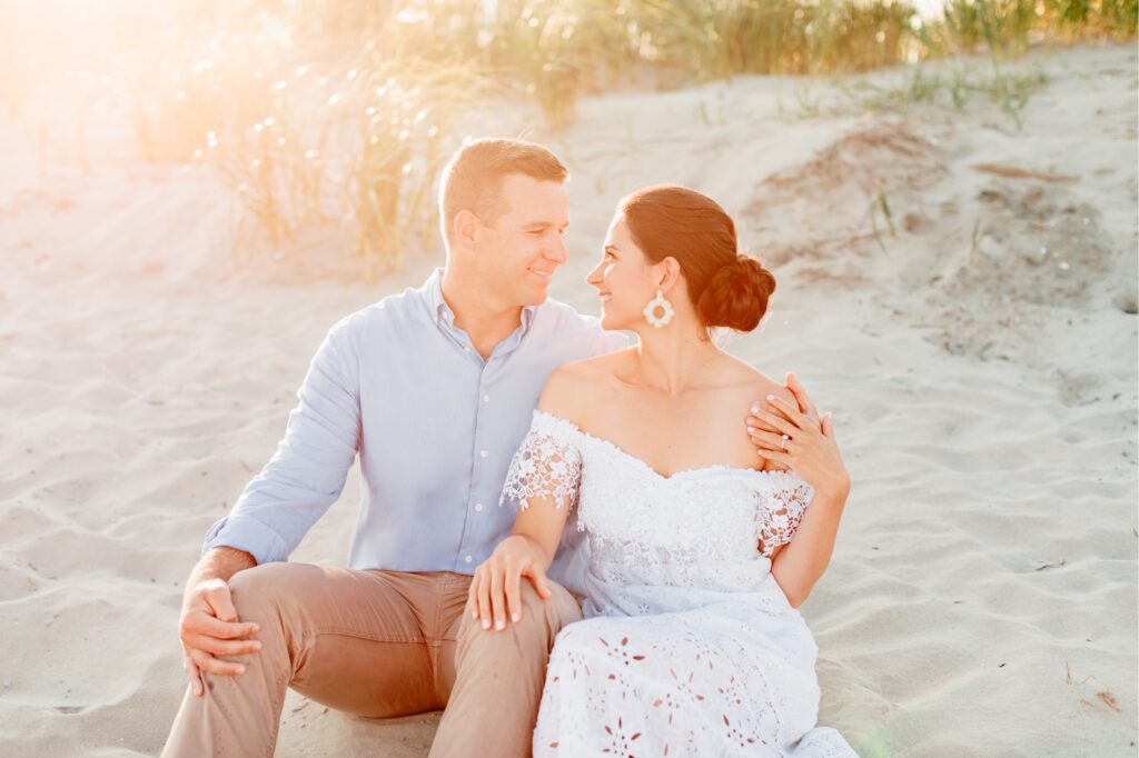 Couple sitting on the sand dunes at sunset for a beach engagement session in NJ