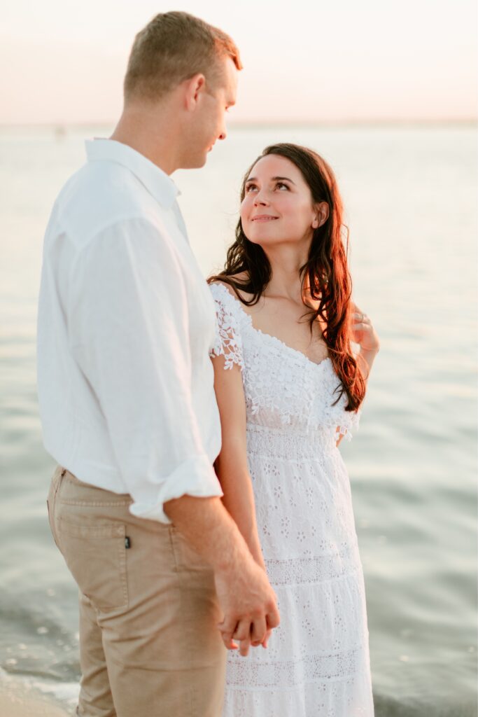 Couple holding hands and lovingly looking at each other during a beach engagement shoot