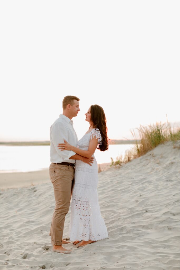 Couple standing on the sand dunes at sunset during a beach engagement session