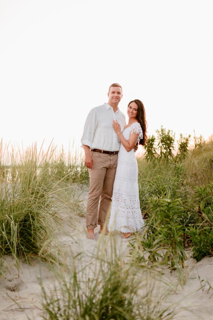 Couple smiling in the sand dunes during a sunset beach engagement session by Emily Wren Photography