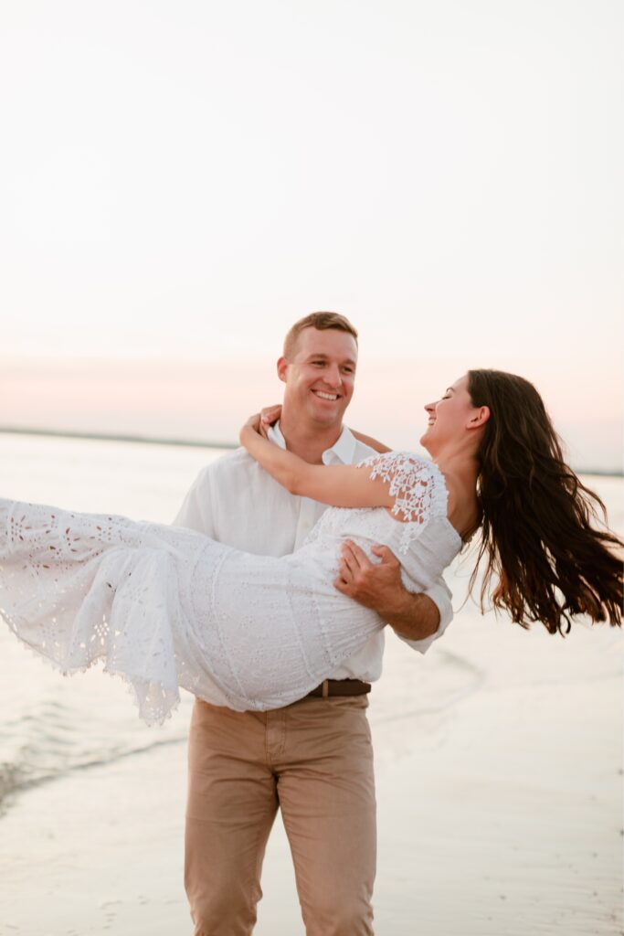 Man holding his fianceé at the Jersey Shore during a beach engagement session