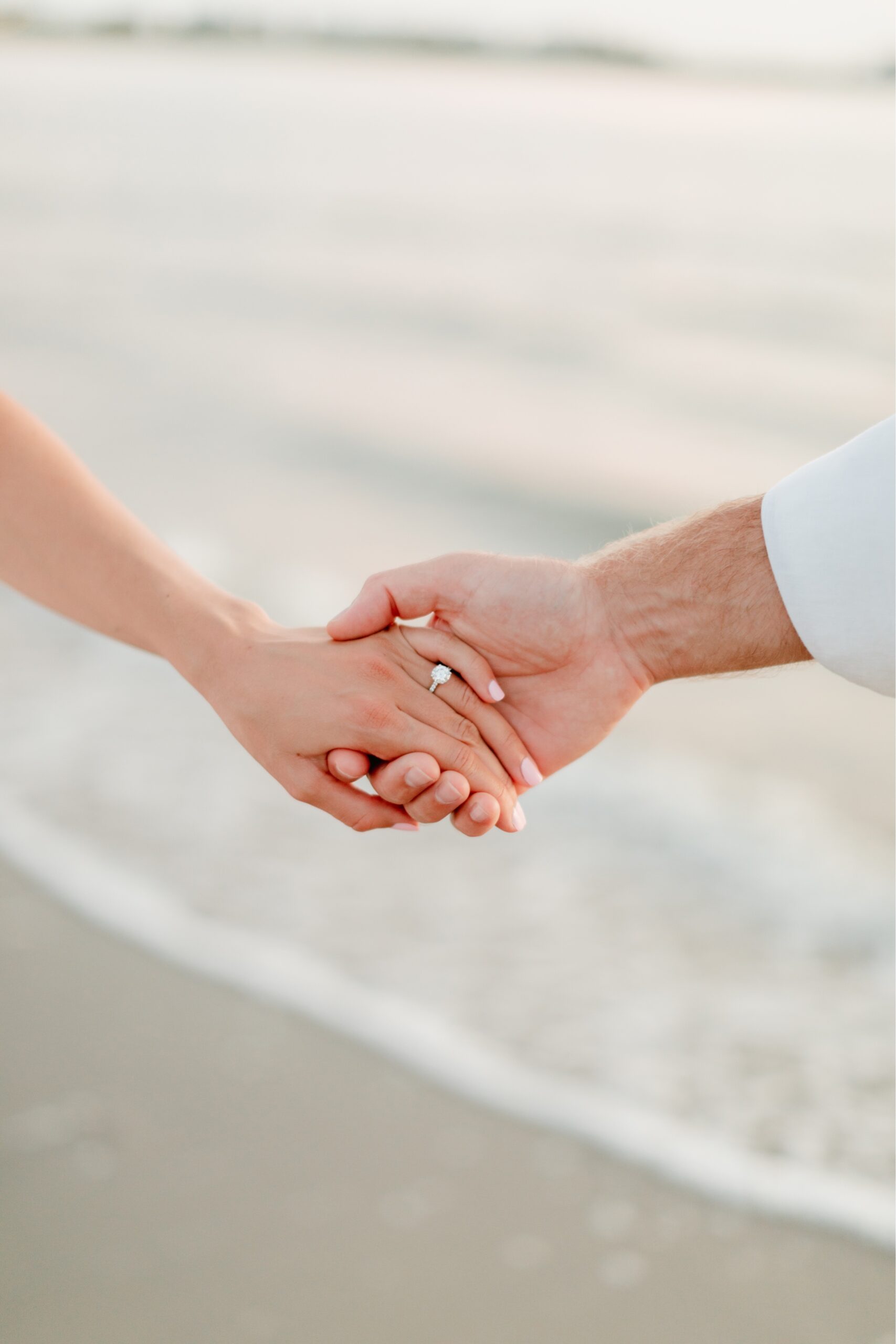 Clasped hands with the ocean in the background by Emily Wren Photography