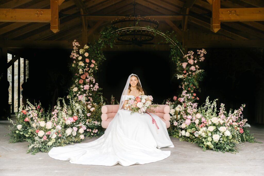 bride surrounded by an arch of greenery, blush, baby pink and white flowers