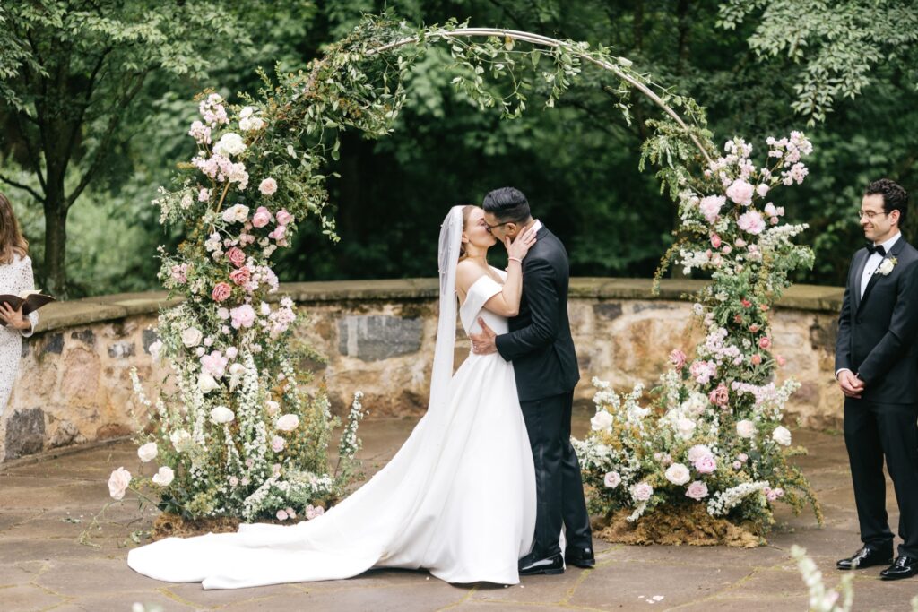 bride and grooms first kiss in front of their spring floral wedding arch