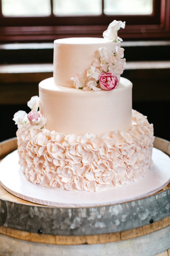 3 tiered pink tinted wedding cake decorated with floral inspired piping and a pink spring flower