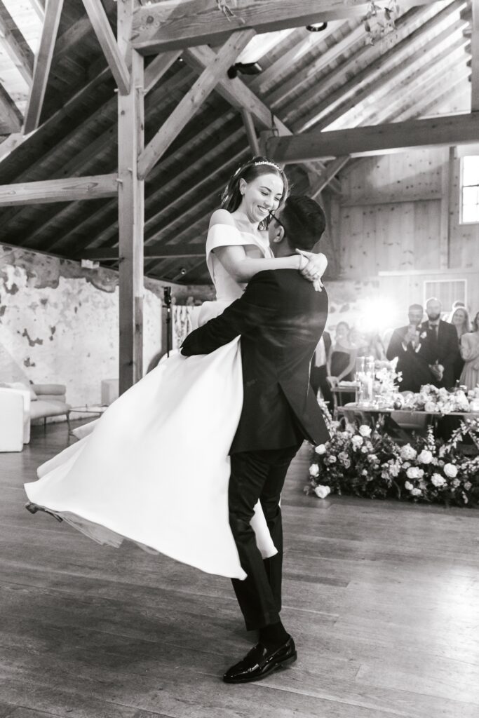 groom lifting bride in a spin during their first dance in their barn wedding reception