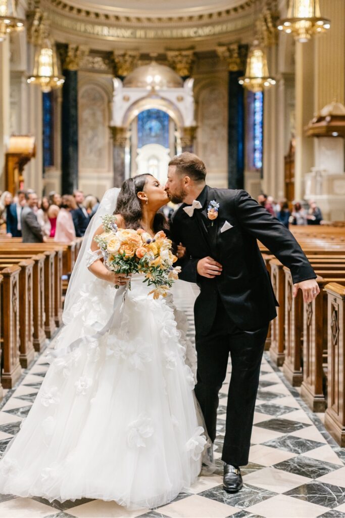 bride and groom kissing at the end of the church aisle after their wedding ceremony