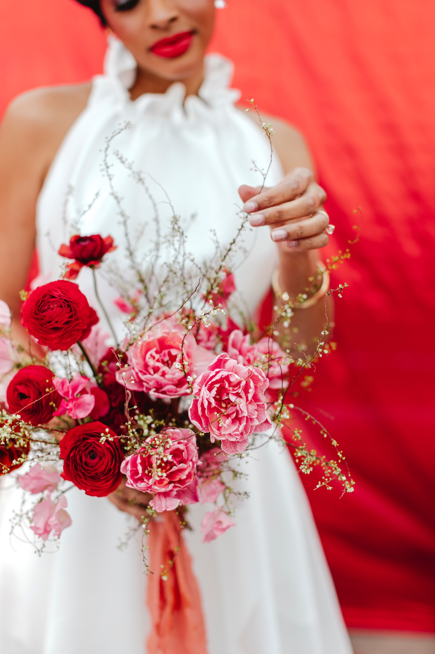 Close-up of a bride holding a bouquet with deep red and pink flowers, with a red backdrop.