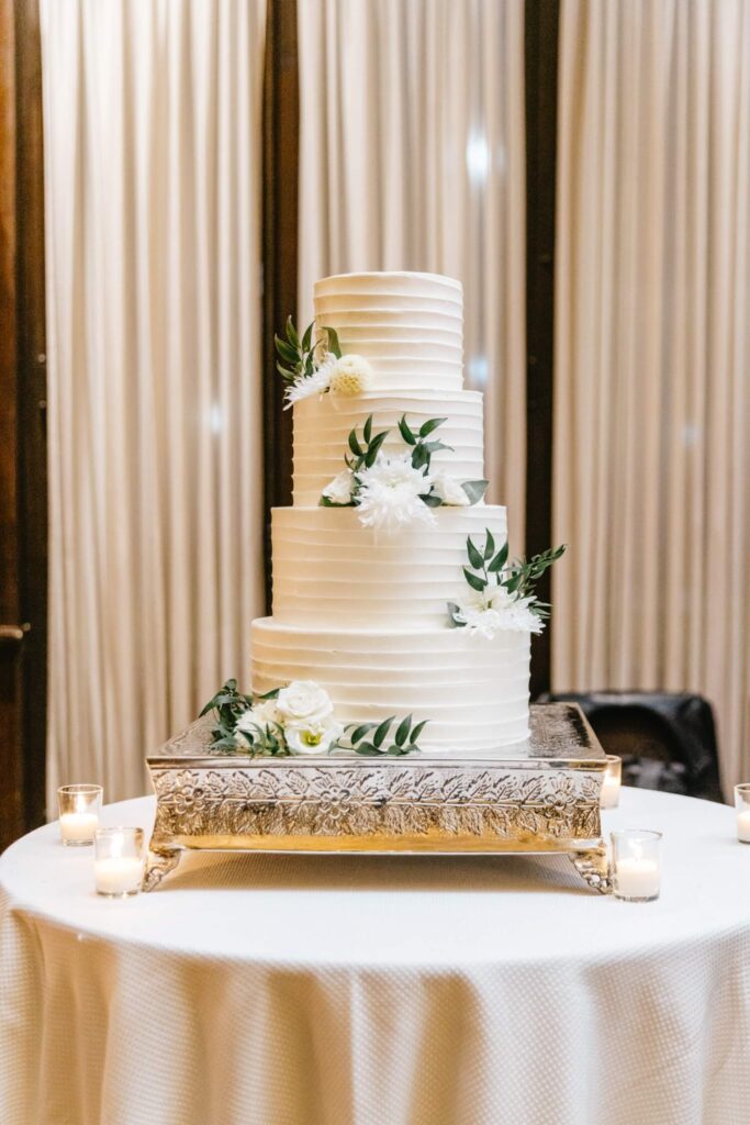 four tier wedding cake with white floral decor and greenery