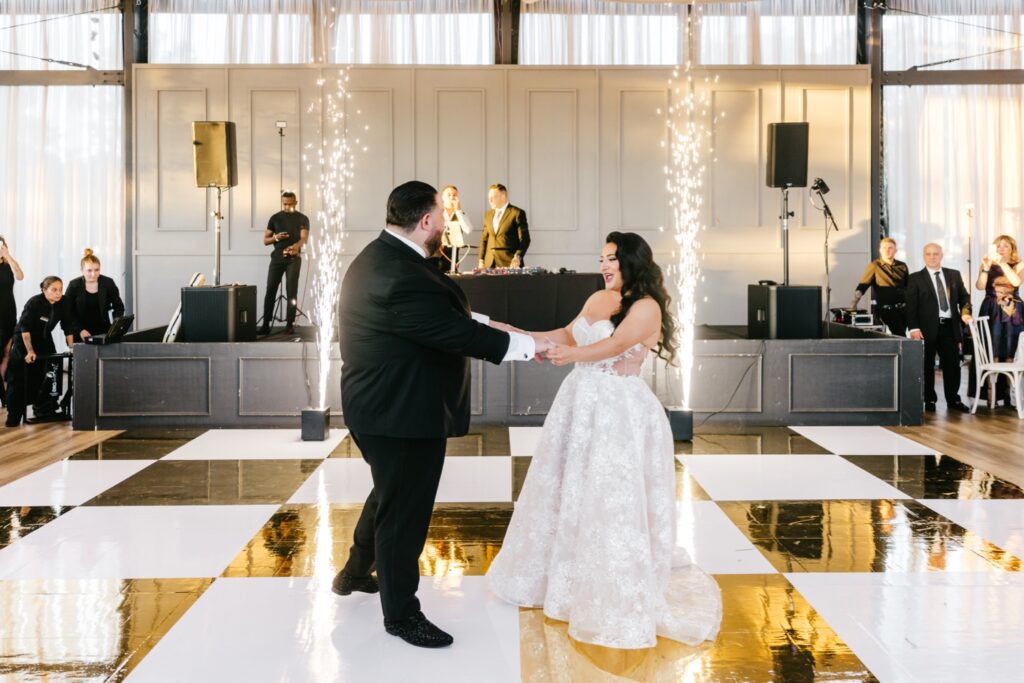 bride & groom's first dance on white & gold checkered dance floor in front of sparklers