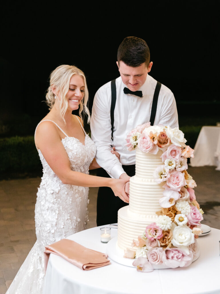 bride & groom cutting wedding cake with pink & white floral decorations