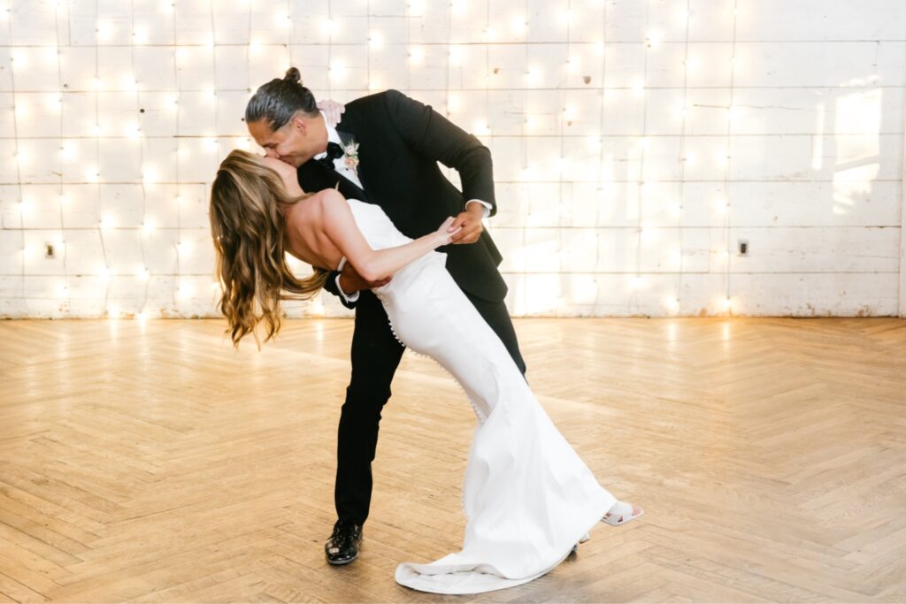 bride & grooms first dance in front of string light wall