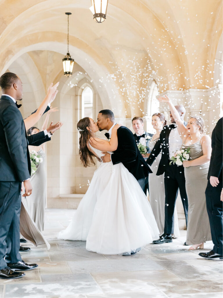 bridal party throwing flower petals on bride & groom as they kiss