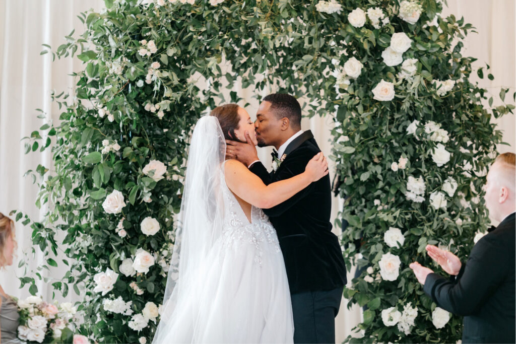 bride & grooms first kiss during Washington dc wedding ceremony i front of white & blush pink floral arch