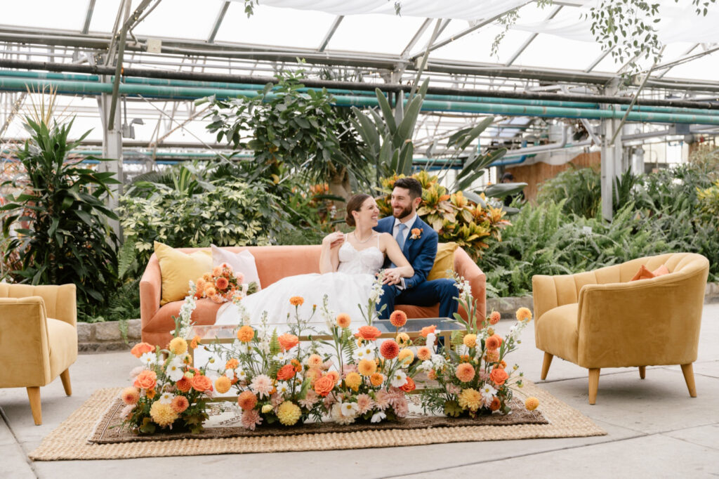 bride & groom sitting on coral cocktail hour lounge couch at Philadelphia Horticultural Center by Emily Wren Photography