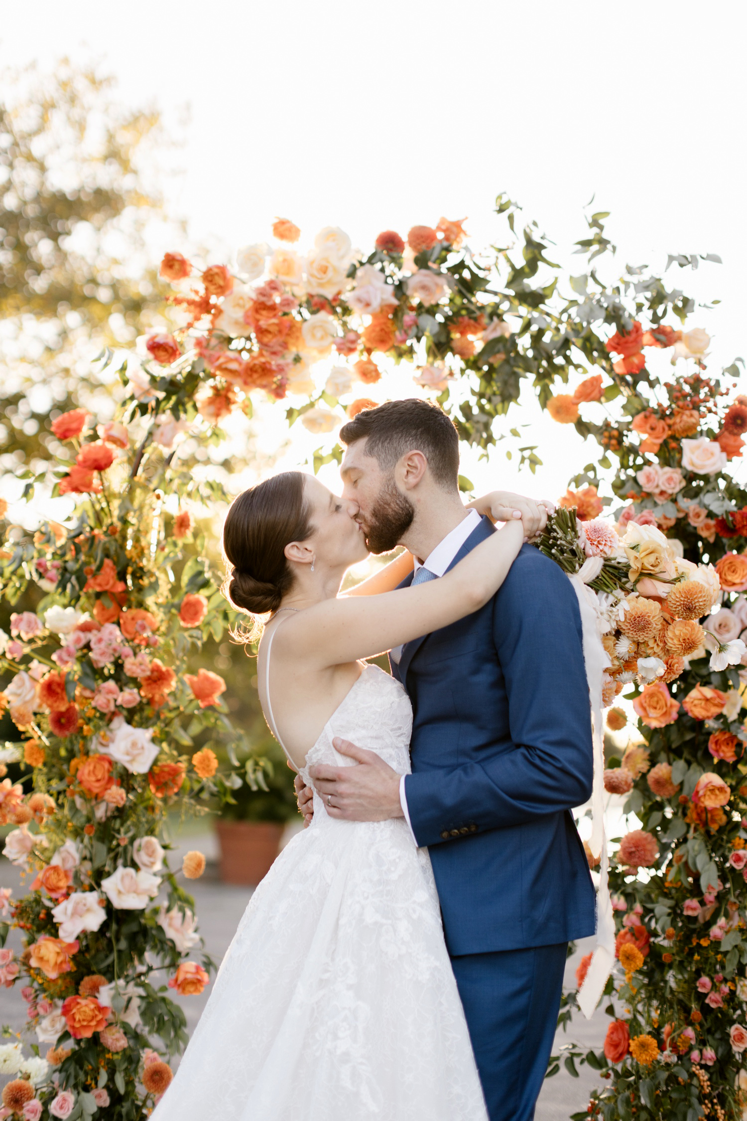bride & groom kissing in front of colorful orange & pink floral arch on their Fall wedding day in Philadelphia