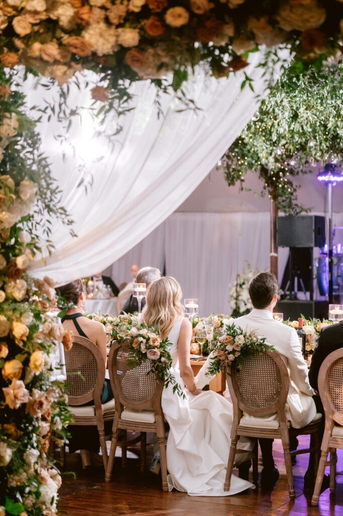 bride & groom listening to bridal party speeches during white tented wedding reception at Radnor Hunt Country Club by Emily Wren Photography